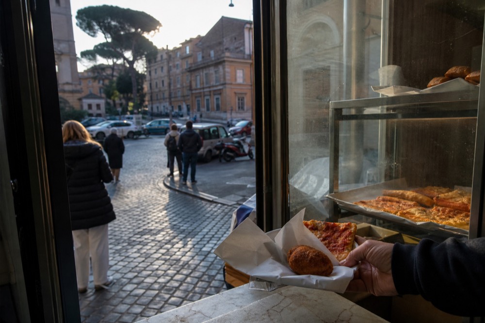 Fried suppli and pizza slices handed over a Roman counter