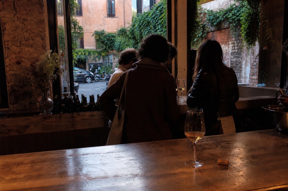 A small group standing at a Trastevere wine counter with glasses poured