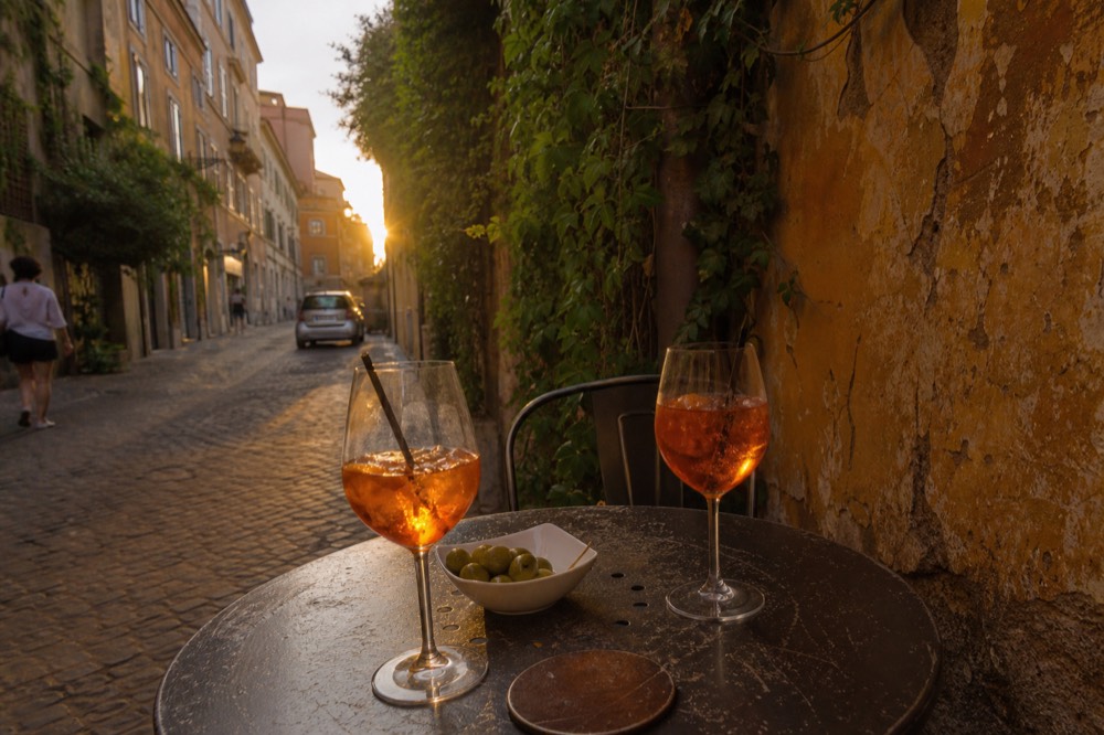 Two orange spritz glasses on a small outdoor table in a Roman side street