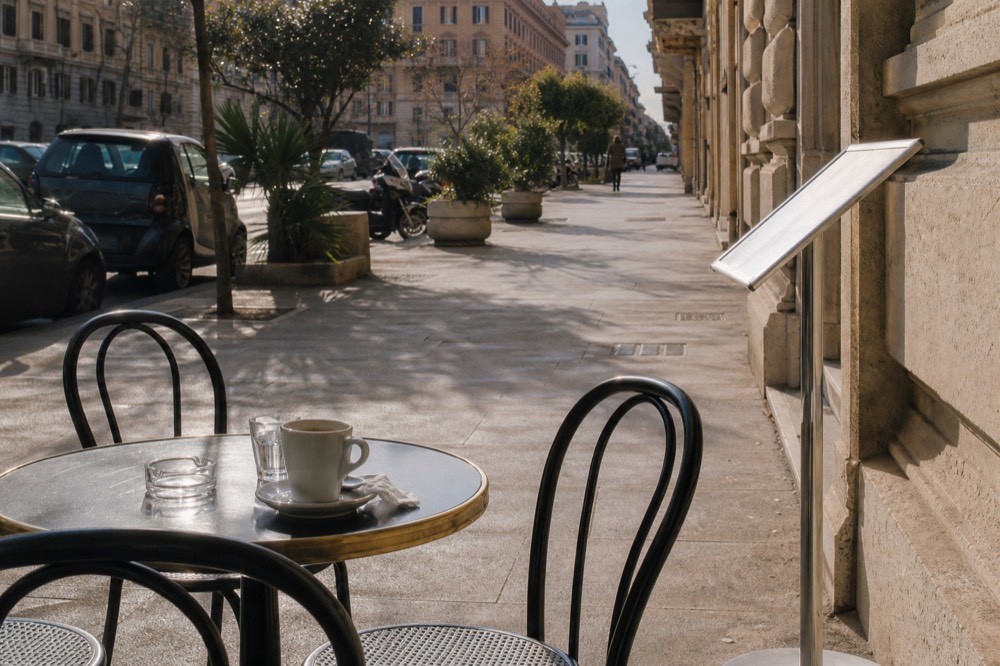 A printed drinks price list clipped to a stand beside an empty cafe table in Rome