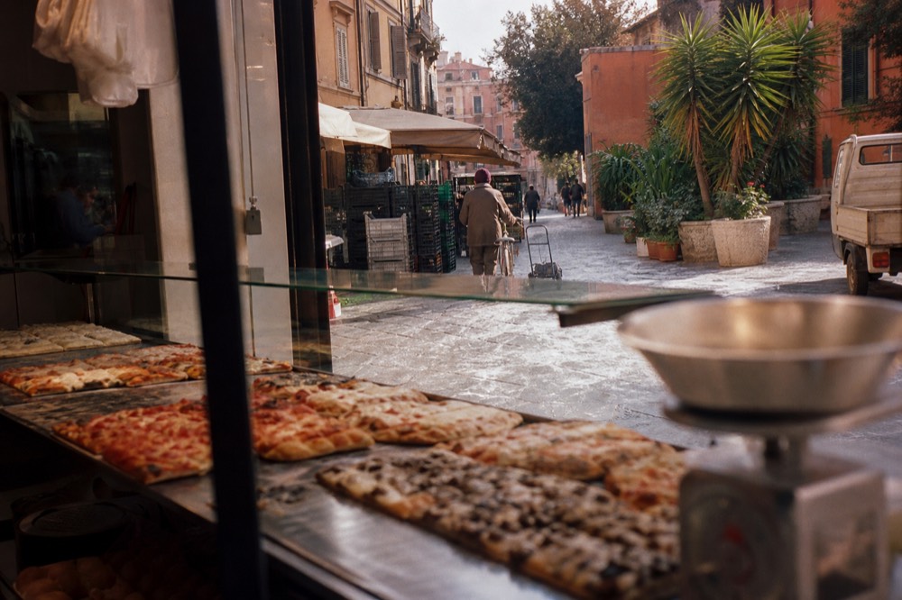 Pizza al taglio trays displayed in a glass counter in Rome