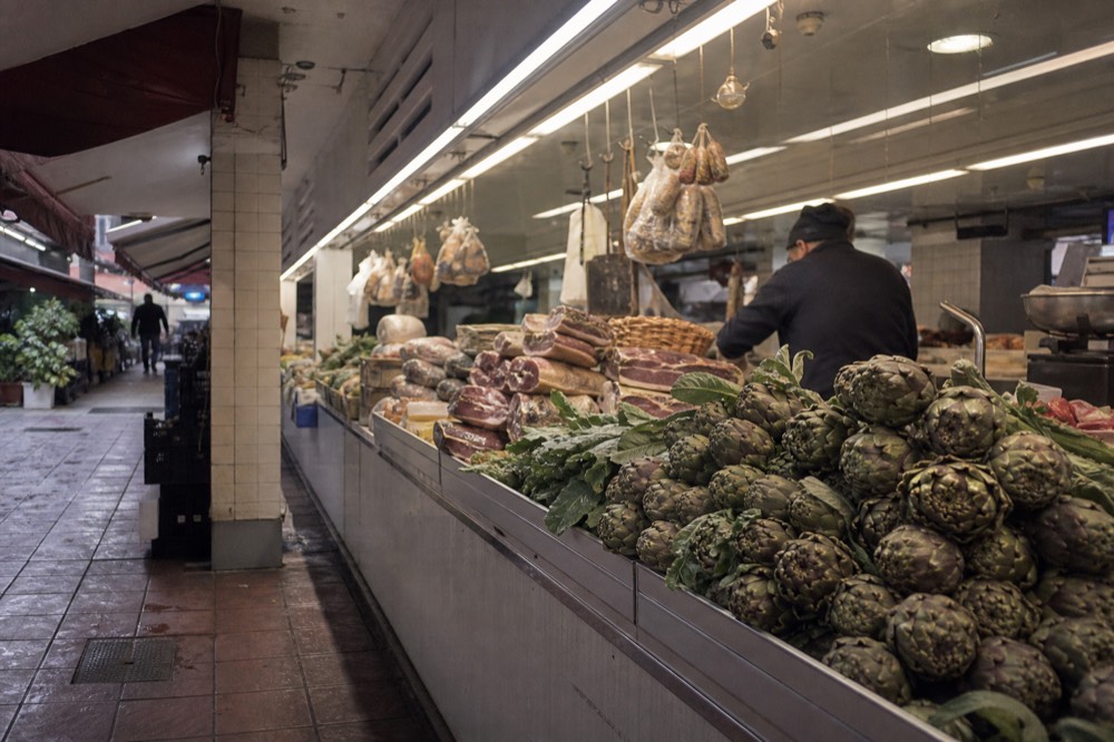 A bustling Roman market hall interior with counter displays of food