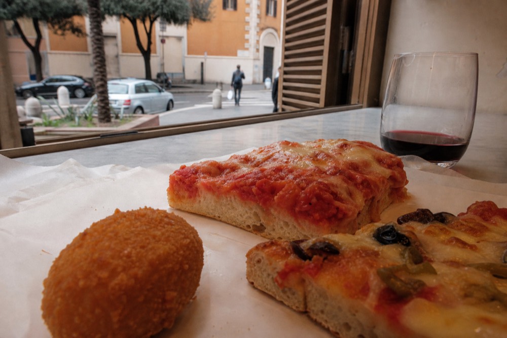 Fried suppli and pizza slices arranged on a paper-lined counter in Rome