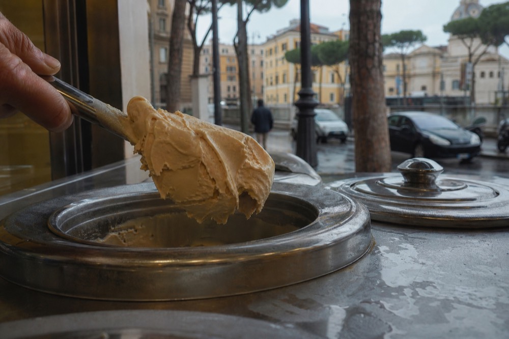 Close view of gelato being scooped from a covered metal tin in Rome