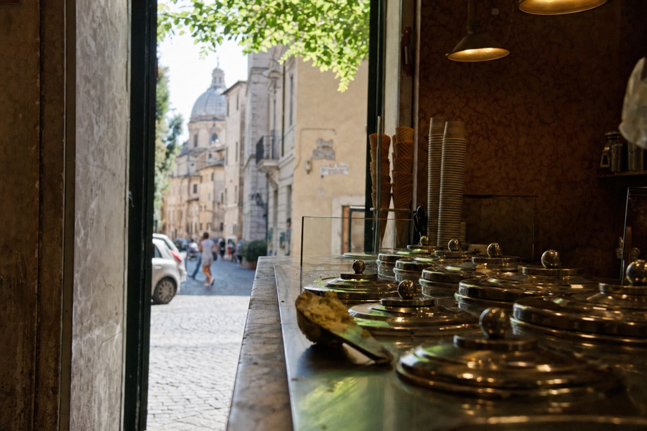 A historic gelateria counter in Rome with rows of covered gelato tins