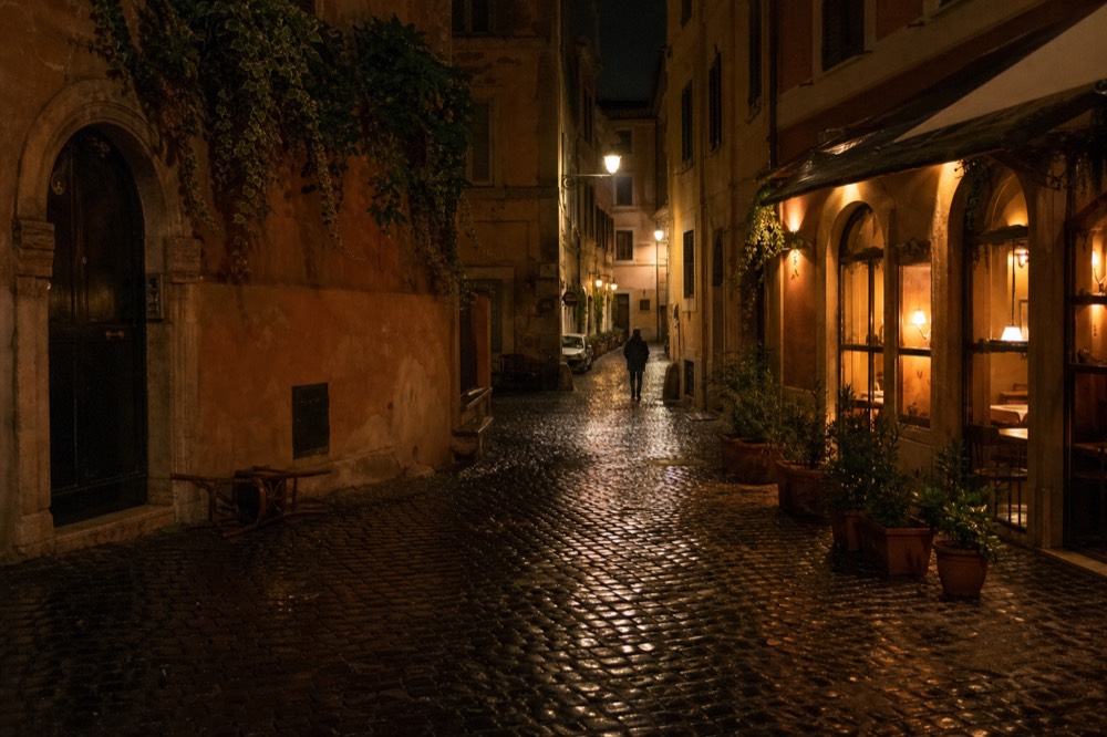 Lit restaurant windows and a quiet cobbled lane in Trastevere at night