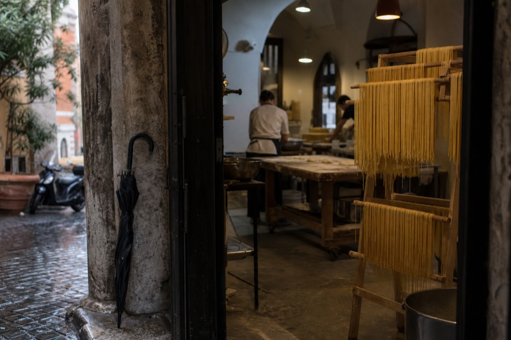 A cooking class kitchen with flour-dusted workbenches and hanging pasta drying on a rack