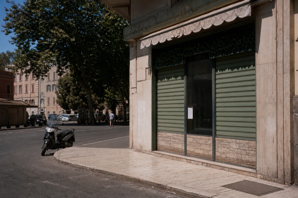 A shuttered Roman restaurant front with a handwritten August closure notice in the window