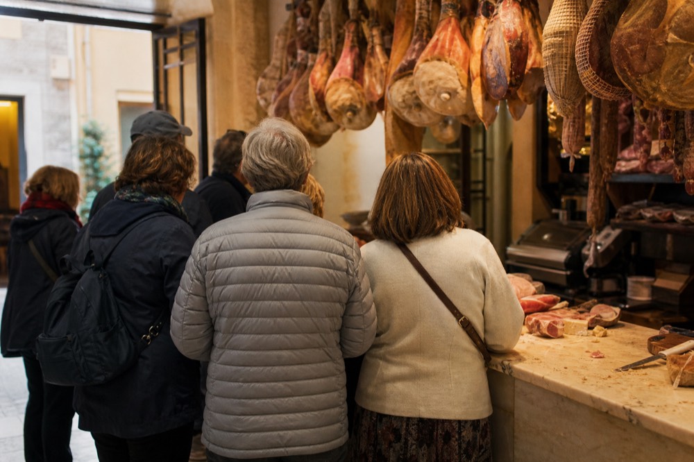 A small-group food tour standing at a counter in a warmly lit Roman food shop