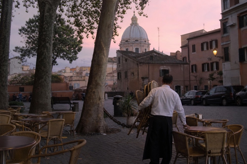A quiet Roman square at dusk in summer with empty outdoor tables