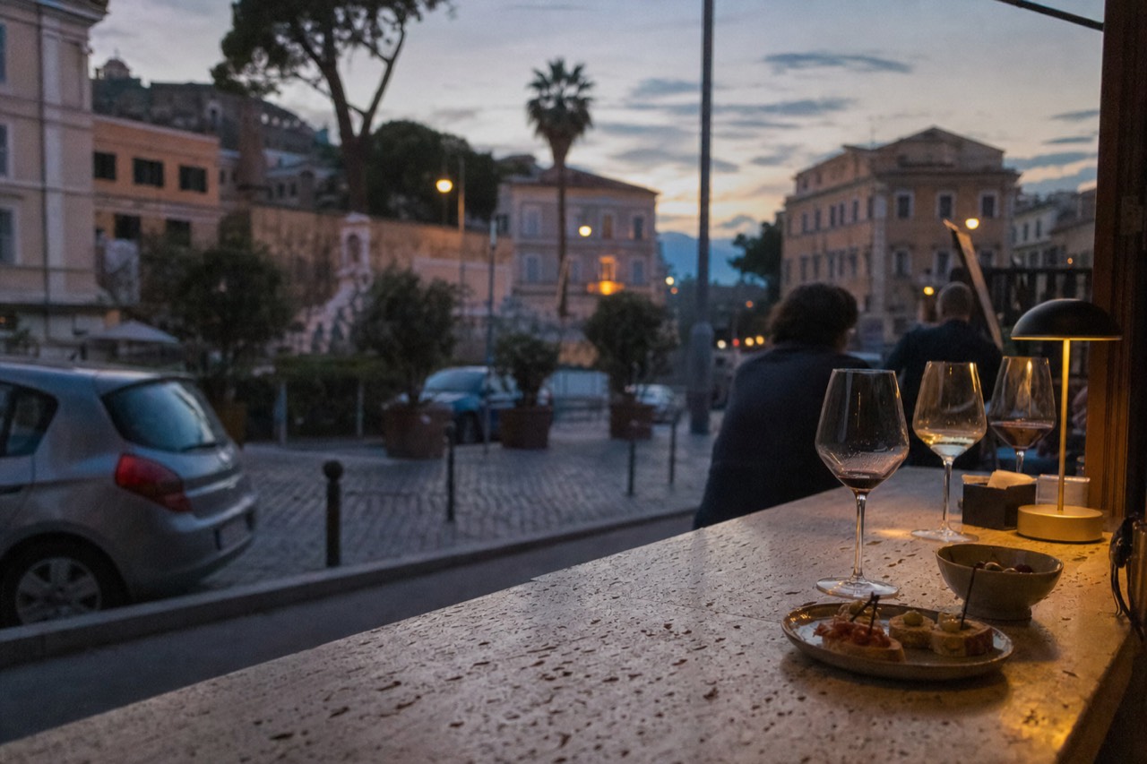 Wine glasses and small snacks on a marble bar counter in Rome at dusk