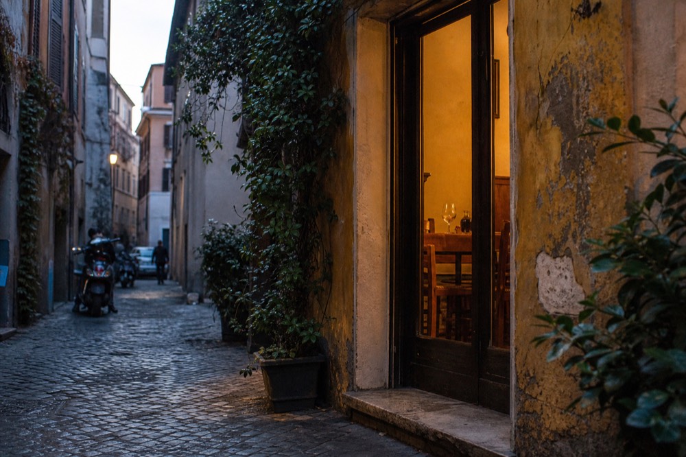 A tiny trattoria doorway in a Trastevere alley with warm light inside