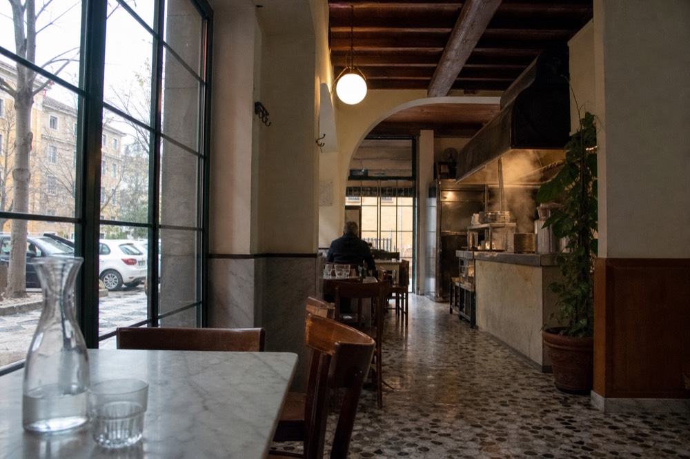 A Roman trattoria dining room with marble-topped tables and a wood beam ceiling