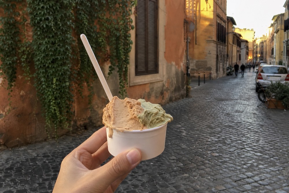 Two natural-coloured gelato scoops in a small cup held in a Roman street