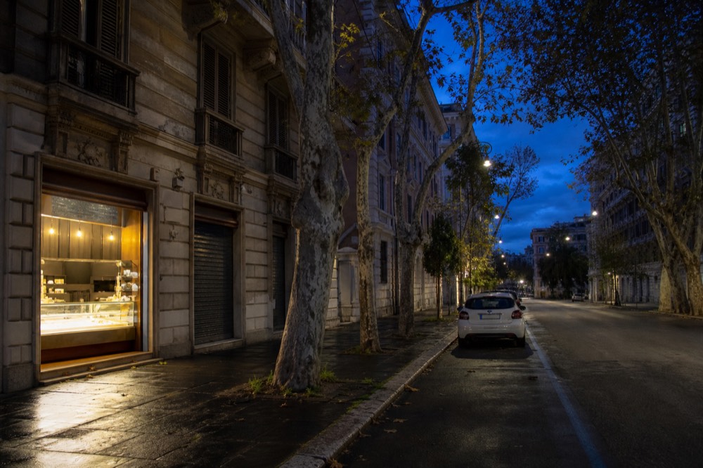 People-free view of a Rome street at dusk with a gelateria window lit