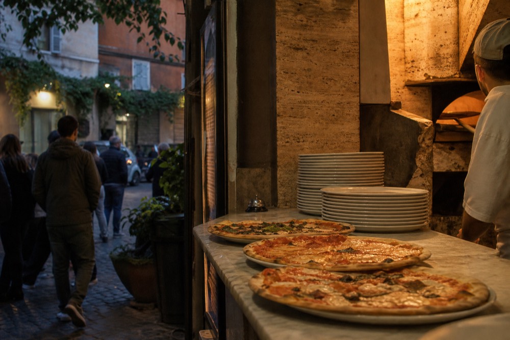 A marble-topped pizzeria counter with pizzas arriving from the oven behind