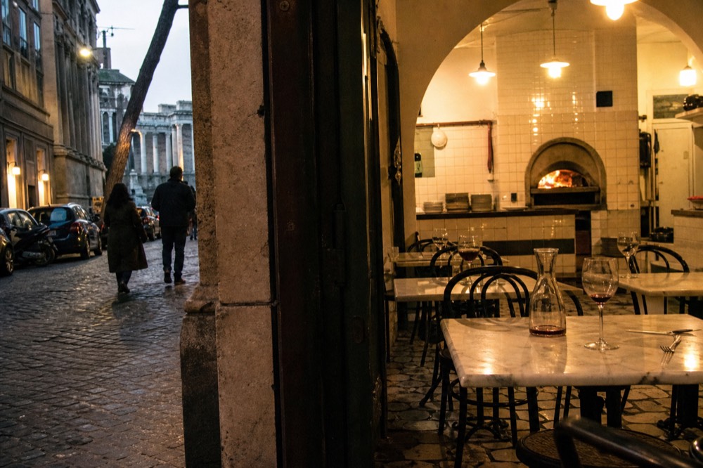 A tiled Roman pizzeria interior with marble tables set for the evening