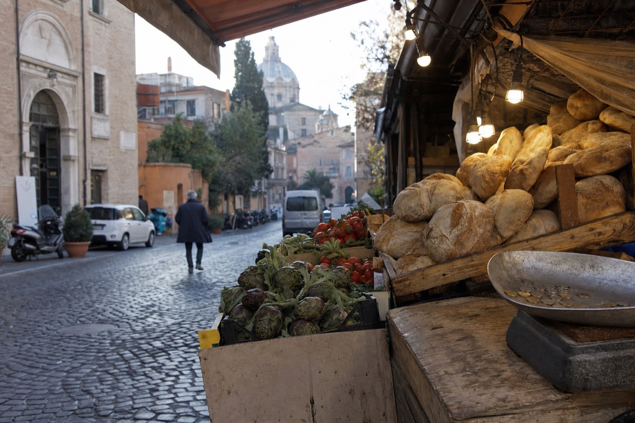 A Roman market stall stacked with bread and vegetables under warm lights