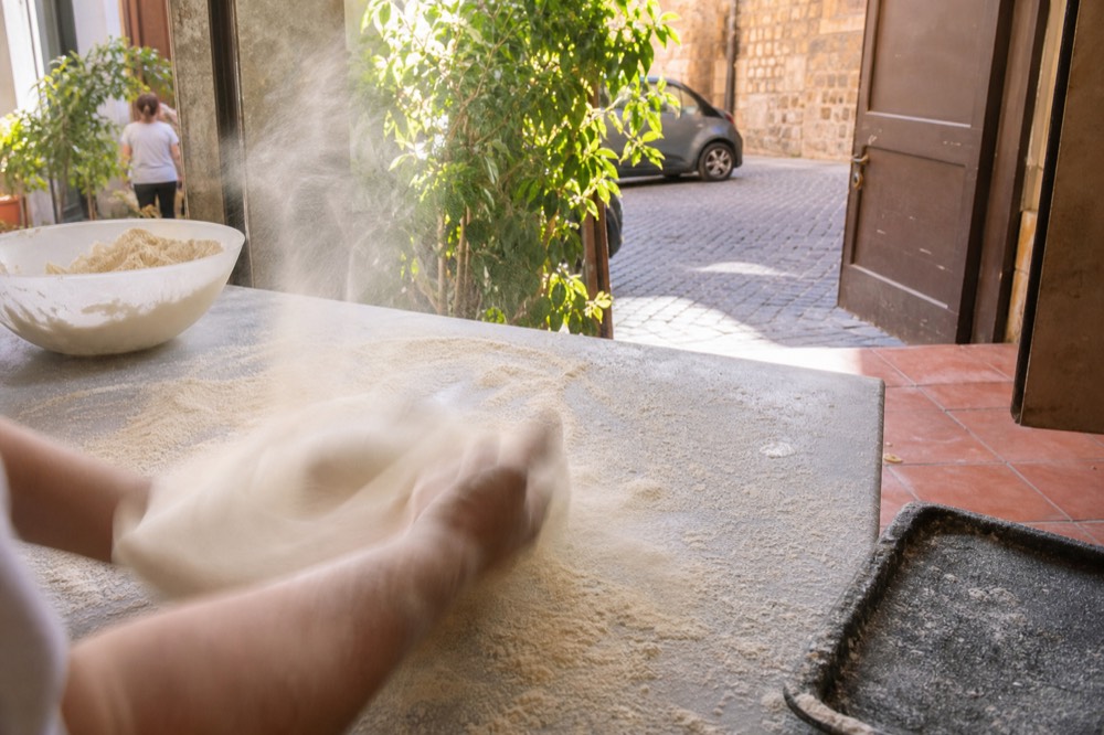 Hands kneading pizza dough on a floured counter in a Rome class kitchen