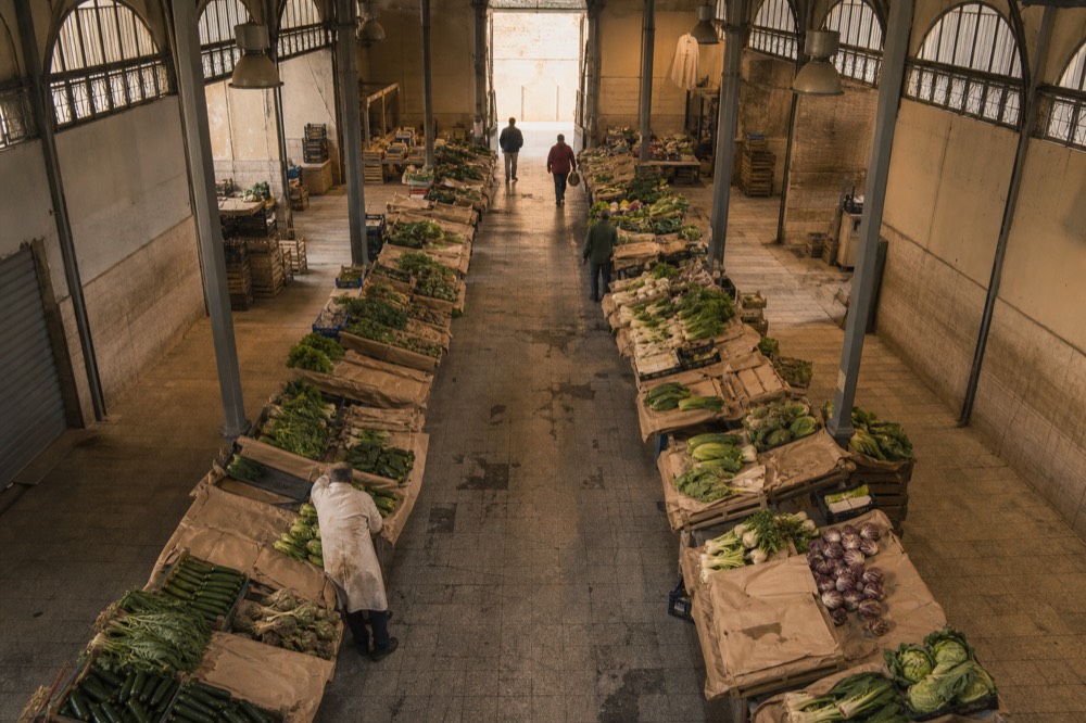 A covered market hall with produce stalls down the aisle