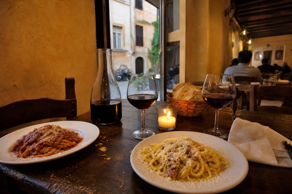 Roman pasta dishes and glasses of red wine set along a wooden Trastevere dinner table