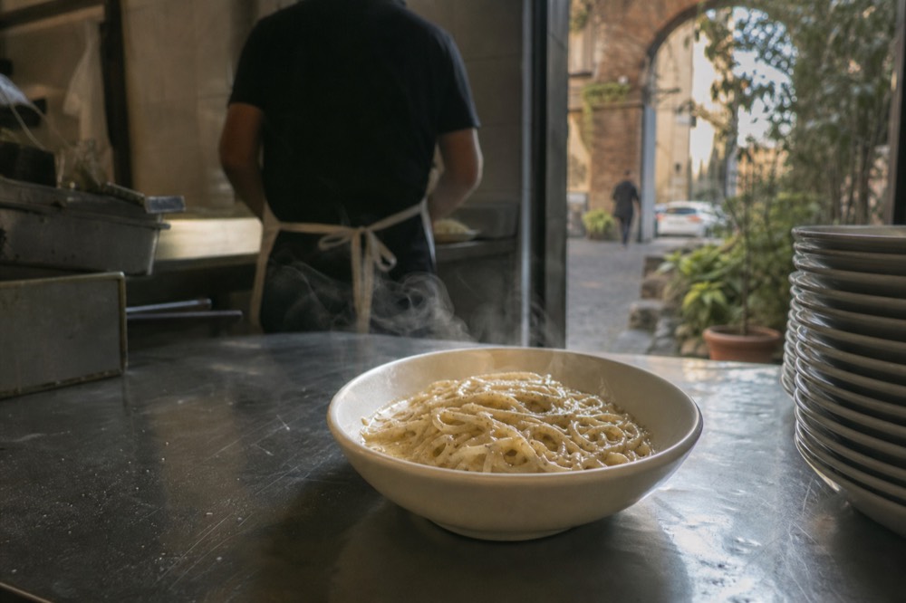 A Roman cook's hands plating a bowl of cacio e pepe pasta