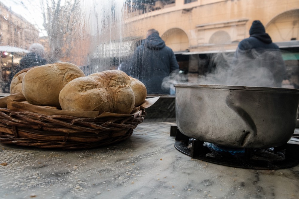 A market stall counter with bread rolls and simmering pots