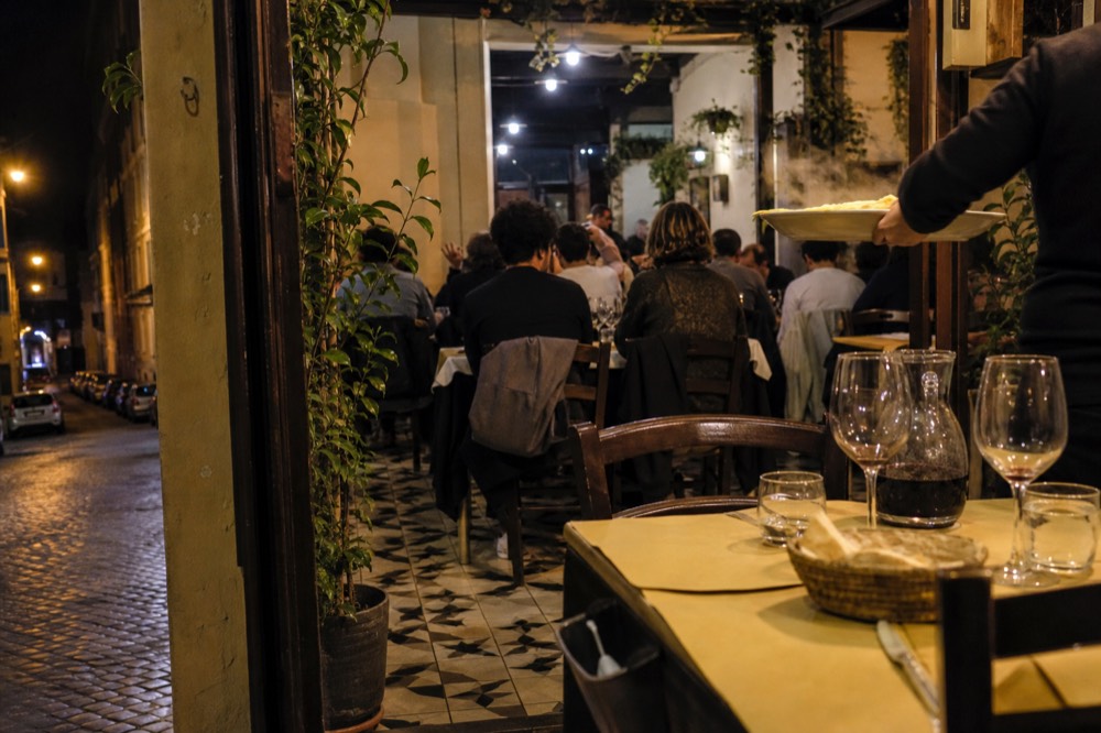 A busy Roman trattoria dining room with tiled floors at night