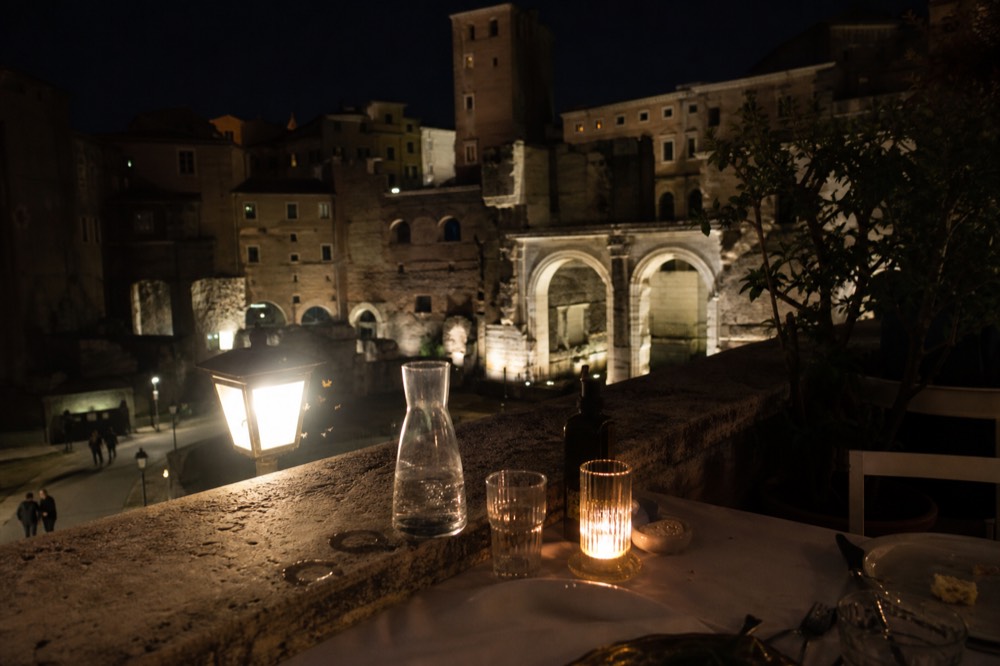 Dinner table on a terrace with the floodlit ruins of ancient Rome beyond