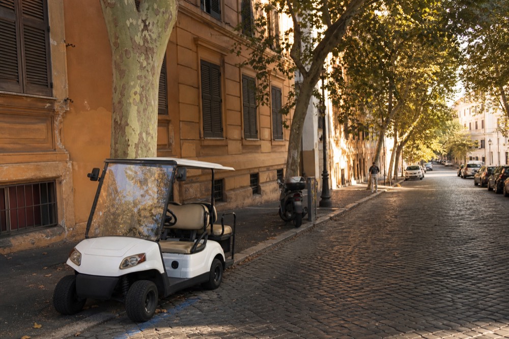 Golf cart parked on a Roman street with a historic facade behind