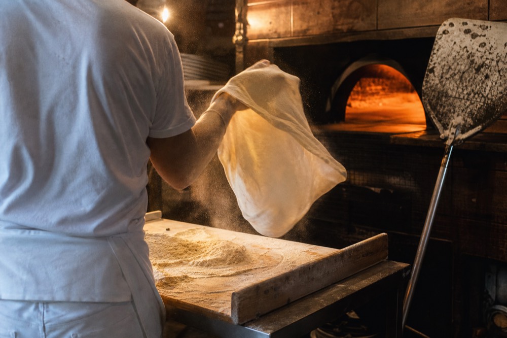 A wood-fired oven with fresh pizza dough being stretched on a counter