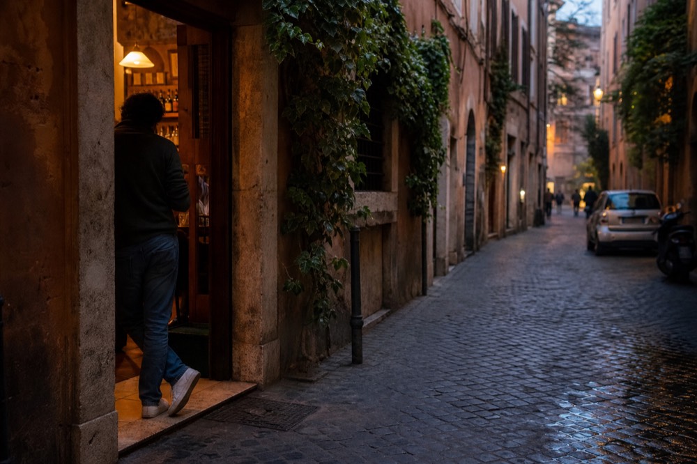 A narrow Roman street at dusk with a lit wine bar doorway