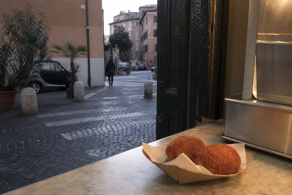 Fresh supplì rice croquettes in a paper tray at a Roman counter