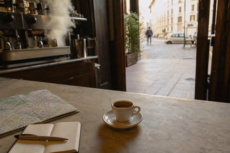 A marble cafe counter in Rome with a small espresso, a folded map and an open notebook beside it
